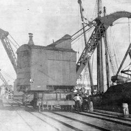 Steam crane loading coal onto ship at Westport wharf.
