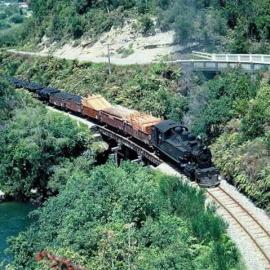 Freight train carrying timber and coal crosses Chasm Creek bridge, Seddonville