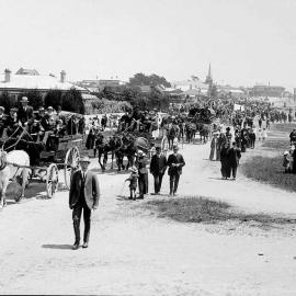 Procession through Hokitika, showing people walking and in horse-drawn wagons.ca.1900.