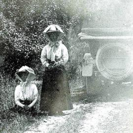 Two women and a car on a West Coast road. 1913.