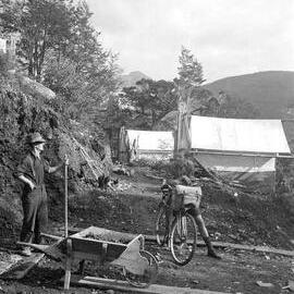 Boy with bicycle talking to man, at construction site in bush.1930.