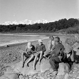Gillespies Beach, South Westland, showing family sitting on rocks. Aug 1953.