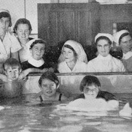 Children recovering from polio in the Greymouth Hospital in a purpose built bath, watched by nurses.1937.