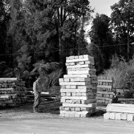 A man standing next to stacked timber in a timber yard at Ross.1947.