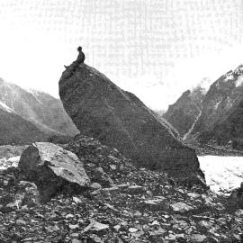 A mountaineer sitting on top of an immense medial moraine rock, which can be seen at the base of the La Perouse Glacier.1912.
