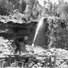 A man directing a high-pressure hose using a makeshift wooden rudder during sluicing operations at a West Coast gold mine.1930`s.