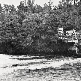 A man standing on a bridge with a waterwheel below - where the Kanieri River runs out of Lake Kanieri,1932.