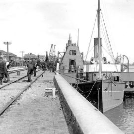 Dockside view showing a small vessel (possibly the Greymouth tug Westland) docked alongside a wharf.ca.1900-1916.