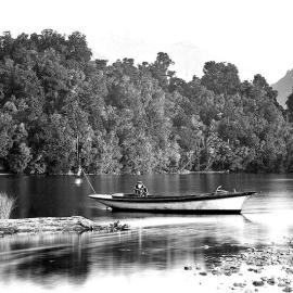A woman  seated in a small vessel moored on a riverbank.Westland.ca.1890`s -1910`s