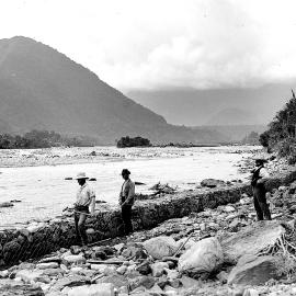 Five people building a stopbank from river stones and wire, Westland